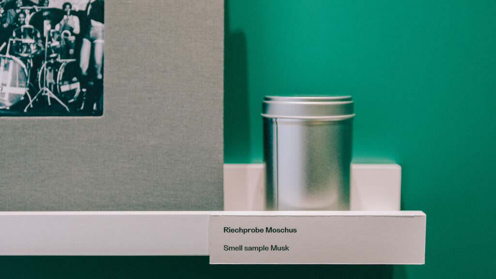 A tin can labeled Smell sample Musk sits on a white shelf in Graz against a green wall.
