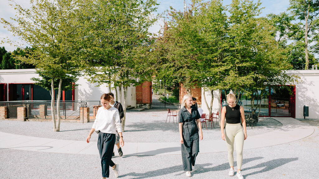 Vier Personen genießen einen sonnigen Rundgang in der Nähe eines Gebäudes mit Bäumen und Sitzgelegenheiten im Freien.
