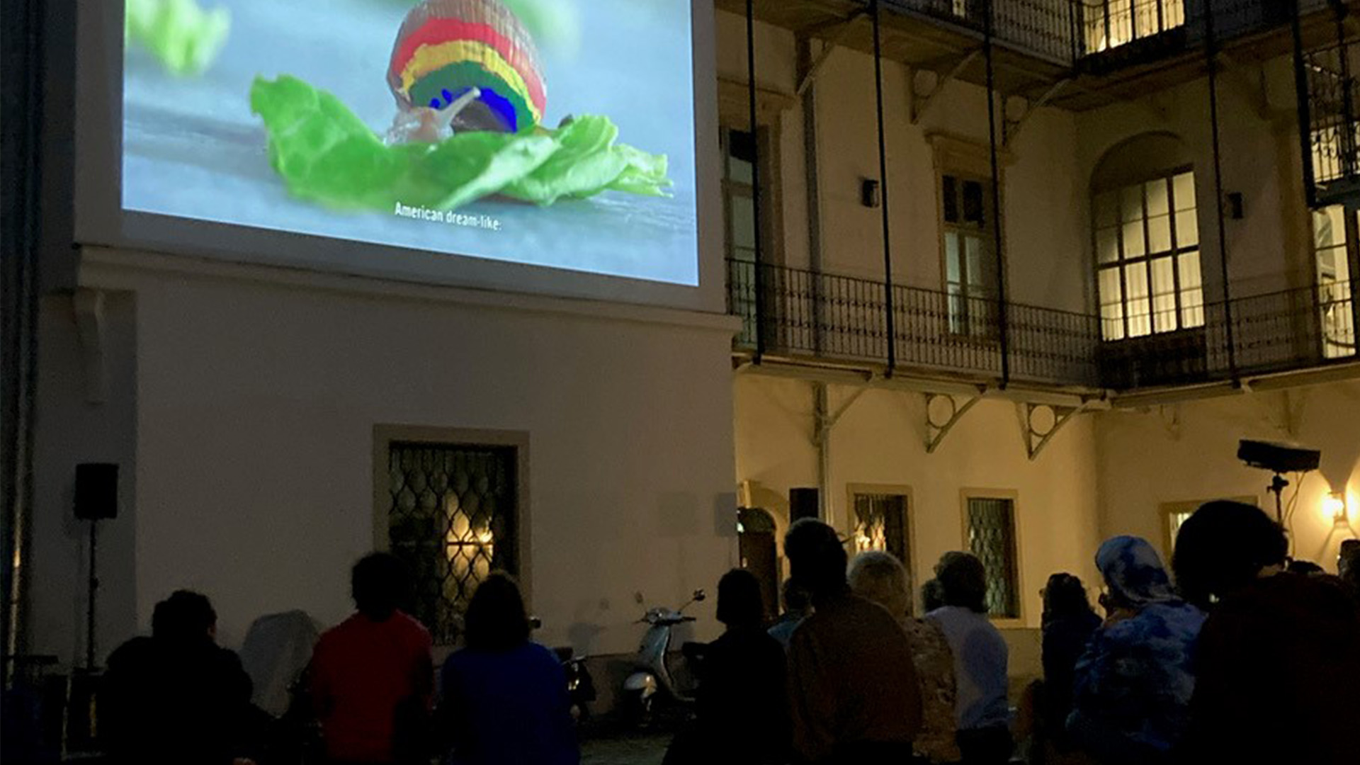 Die Menschen schauen sich nachts einen Film des „Sunset Cinema“ an, der auf eine Hauswand projiziert wird.
