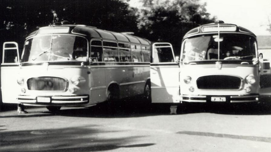 Zwei Oldtimer-Busse, die nebeneinander mit offenen Türen geparkt sind; Schwarz-Weiß-Foto.