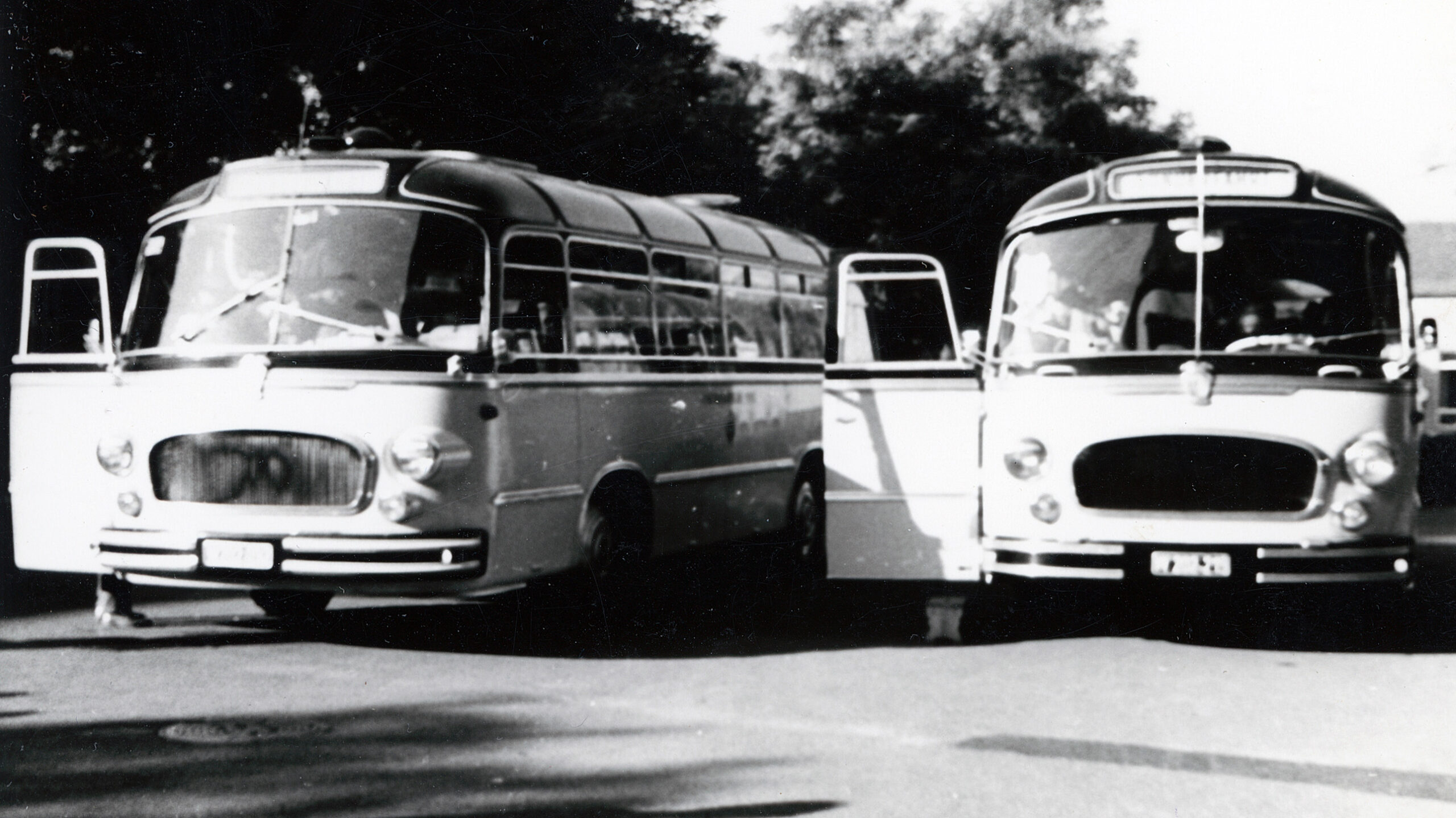 Auf einem Schwarz-Weiß-Foto stehen zwei Oldtimer-Busse nebeneinander, deren Vordertüren geöffnet sind.
