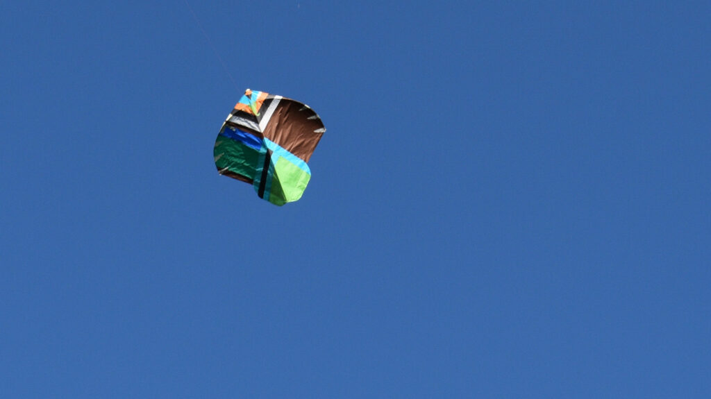 Ein bunter Drachen aus dem Drachenbau-Workshop schwebt über dem strahlend blauen Himmel des Schlossbergs.