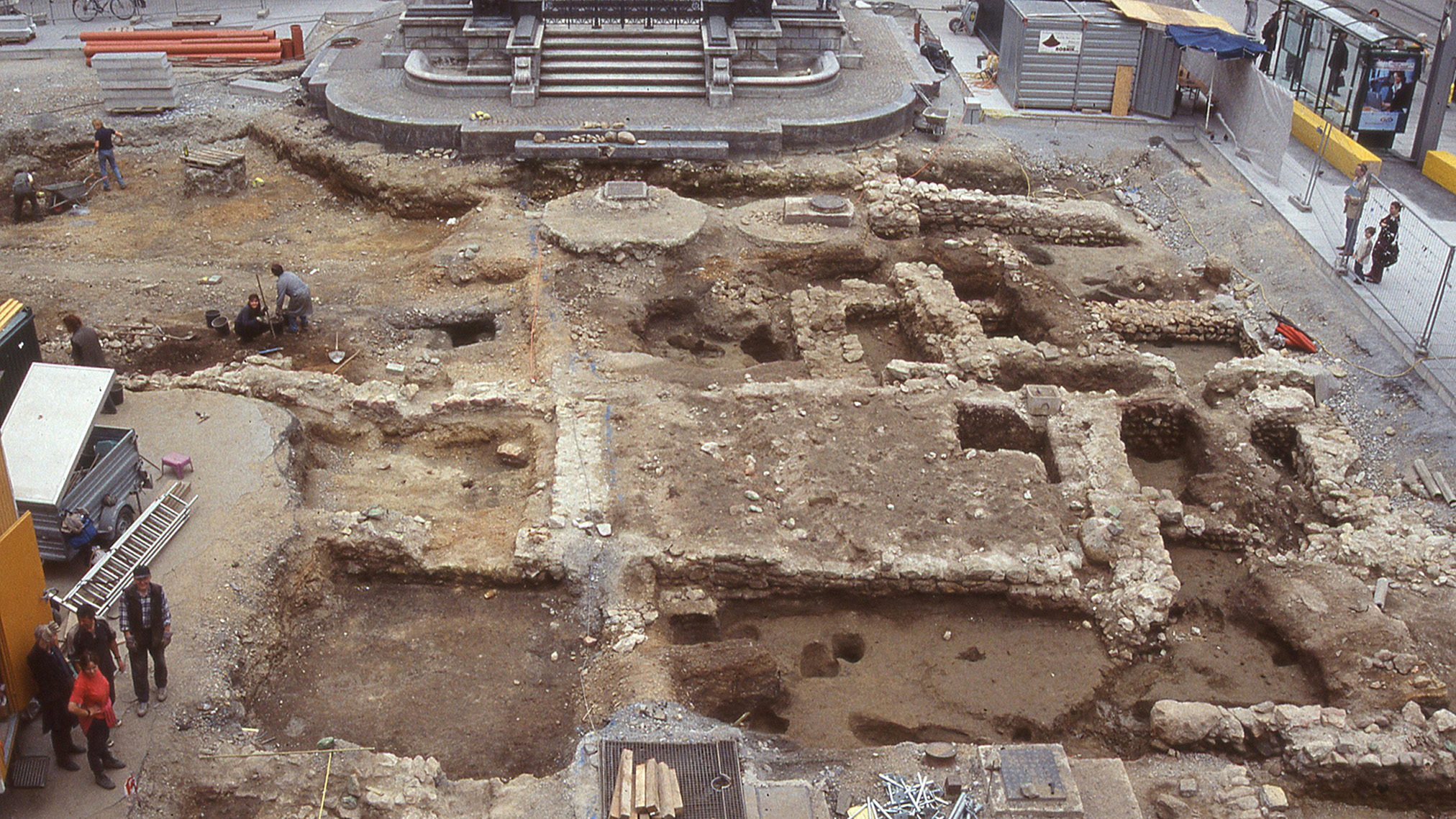 Luftaufnahme einer archäologischen Ausgrabungsstätte in Graz, auf der Arbeiter im Erdreich graben.